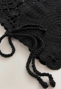 Černá háčkovaná látka s kruhovým vzorem, zdobená pletenými tkaničkami a krajkovými okraji. Textura vypadá měkce a složitě.