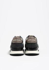 Pair of black and gray sneakers with white soles, viewed from the back, showing "BIMBA Y LOLA" branding on the heel tabs.