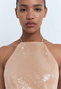 Top halter de color nude con superficie texturizada de lentejuelas, que presenta tirantes finos y una silueta ajustada.