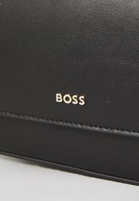 Accessorio in pelle nera con finitura testurizzata, caratterizzato da un logo dorato "BOSS" e dettagli cuciti lungo i bordi.