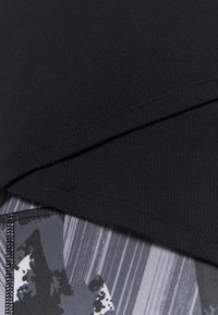 Czarny prążkowany materiał nachodzi na szary, wzorzysty materiał z abstrakcyjnymi kształtami i pionowymi liniami. Teksturowane detale podkreślają wzór.