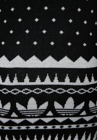 Zwart-wit gebreide stof met een geometrisch patroon van sterren, bergen en bloemaccenten, wat een contrasterende textuur creëert.