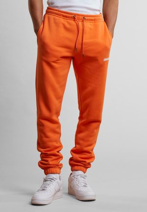 Bright orange jogger pants in a soft material, featuring an elastic waistband with drawstring, cuffed ankles, and side pockets.