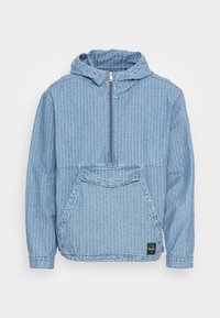 Ljusblå denimpulloverjacka med dragkedja fram, huva och stor framficka. Har vertikal ribbad textur och uppvikta ärmar.