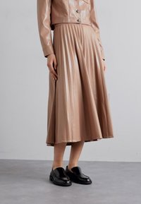 Ljust brunt plisserat klänning i konstläder med en figursydd överdel, silverknappar och en slät textur, kombinerad med svarta loafers.