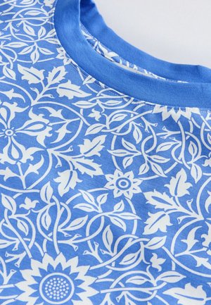 Blaue Baumwollstoffe mit floralen Mustern in Weiß, die Blätter und Blumen zeigen. Runde blaue Ausschnitt. Weiche, glatte Textur.