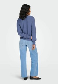 Blauwe geribbelde trui met lange mouwen, gecombineerd met lichtblauwe wijd uitlopende jeans. De outfit wordt afgewerkt met zwarte platte schoenen en straalt een casual look uit.