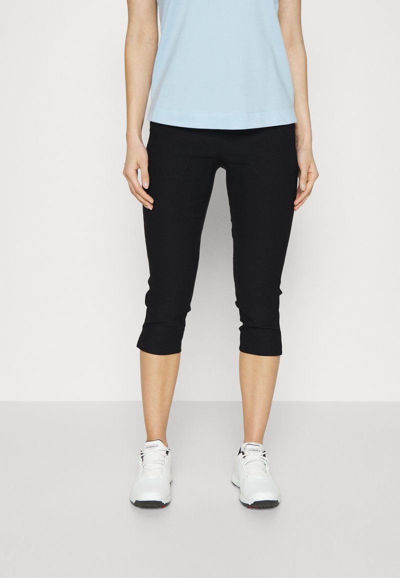 Leggings capri pretos com um design ajustado, apresentando uma textura suave e um comprimento cortado, combinados com tênis atléticos brancos.
