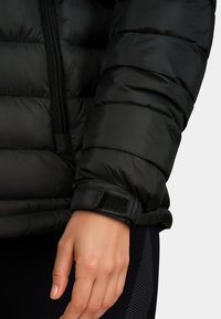 Czarna kurtka puchowa z pikowanymi sekcjami, wyposażona w zamek błyskawiczny i regulowane mankiety na rzep. Gładka tekstura i ocieplana konstrukcja.