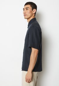 Korte mouwen, marineblauwe shirt van lichte stof met een button-down kraag en een borstzak. Soepele textuur en relaxte pasvorm.