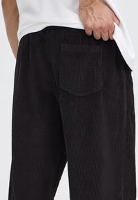 Pantaloni din catifea neagră cu dungi verticale, cu buzunar în spate. Materialul are o textură moale și un design ușor relaxat.