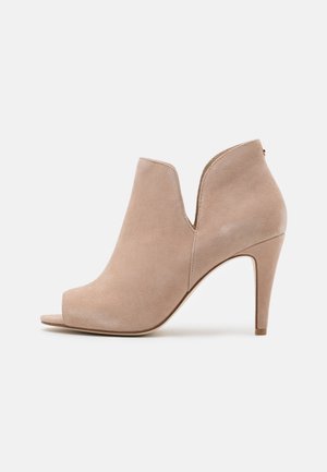 Beige ruskindsankelstøvle med åbent tådesign, udskæringer og høj stilethæl. Glat tekstur og elegant silhuet.