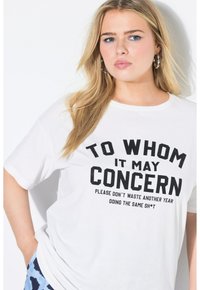 Wit katoenen T-shirt met zwarte tekst "TO WHOM IT MAY CONCERN" op de voorkant. Korte mouwen en een ronde hals, losse pasvorm.
