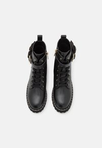 Botas de tobillo de cuero negro con herrajes dorados, diseño de cordones y acentos de tachuelas a lo largo de la suela. Detalles de ante en los laterales.