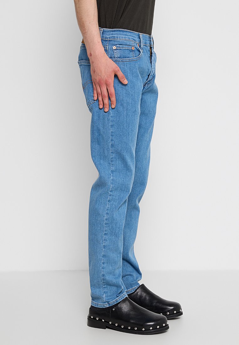 Jean en denim bleu clair avec une coupe droite, design à cinq poches et décoloration subtile. Porté avec des sabots noirs ornés de clous en argent.