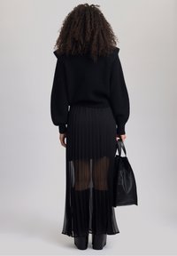 Pull noir en tricot avec des manches bouffantes, associé à une jupe noire plissée avec une superposition transparente. Complété par des bottes noires jusqu'aux genoux et un sac.