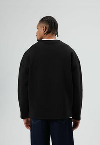 Zwarte oversized sweatshirt met een ronde hals, vallende schouders en geribbelde manchetten, gecombineerd met losse donkere spijkerbroek.