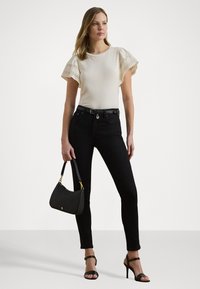 Cream short-sleeve top with lace detail, black skinny jeans, black handbag with gold accents, and black strappy heels.