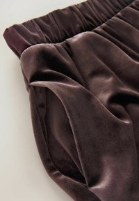 Tamsiai rudas veliūro audinys su švelniu blizgesiu, turintis surinktą liemens juostą ir laisvai krentantį drapą, rodantis lygią tekstūrą ir prabangų vaizdą.