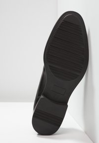 Semelle de chaussure en cuir noir avec des rainures horizontales et un bout arrondi. Présente une finition lisse et un détail rectangulaire près du talon. Taille 42.