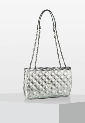 Gewatteerde metallic zilveren schoudertas met kettingbandjes en driehoekig Guess-logo op de voorflap, tentoongesteld op een wit voetstuk.