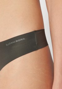 Tanga Björk Borg en tissu vert foncé ; texture lisse avec un design minimaliste. Présente une marque sur la ceinture.