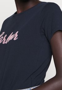 Navyblauwe katoenen T-shirt met korte mouwen, voorzien van een roze scriptontwerp aan de voorkant. Zachte textuur, ronde halslijn en casual pasvorm.