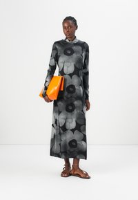 Long-sleeve black dress with large gray floral pattern, accompanied by an orange glossy clutch bag. Model wears brown strappy sandals.