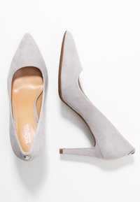 Escarpin en nubuck gris à talons hauts avec un embout pointu et un design découpé. Semelle intérieure en cuir lisse et semelle en caoutchouc brun clair avec un petit détail d'accent.