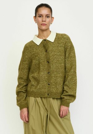 Olivovo zelený kardigán s béžovým golierom, zapínaním na gombíky vpredu a rebrovanými manžetami. Mäkká textúra a voľný strih. Nosený cez svetlozelené nohavice.