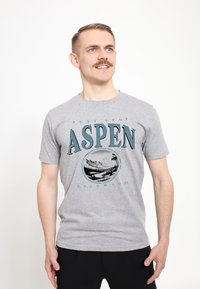 Camiseta de algodón gris con el texto "ASPEN" en azul oscuro, con un gráfico circular de montañas y árboles debajo. Mangas cortas y cuello redondo.