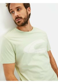 Lys grøn kortærmet t-shirt med et stort hvidt logo på fronten. Stoffet ser glat ud med en afslappet pasform.