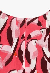 Kolorowa tkanina sukienkowa z różowym tłem i abstrakcyjnymi wzorami ptaków w białym i ciemnoczerwonym kolorze, z widocznym zapięciem na zamek z tyłu.