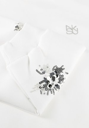 Witte sokken met geribbelde boordjes, voorzien van zilveren en zwarte pailletten bloemenpatronen en een klein zilveren monogram op de stof.