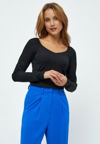 Zwarte lange mouwen top met een vierkante halslijn, gecombineerd met blauwe hooggetailleerde broek met plooien en zijzakken. Gladde stoftextuur.