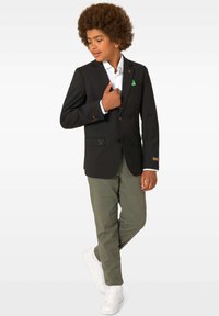 Melnā uzvalka žakete ar krāsainiem izšuvuma akcentiem, balta krekls, zaļš kabatas lakatiņš, olīvu krāsas bikses un baltas kedas. Šaurs piegriezums.