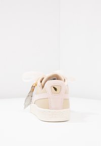 Baskets rose clair avec des matériaux en daim et cuir, grandes lacets en forme de nœud, accessoires en or et une semelle en caoutchouc blanc texturé. Présente un accent en forme de feuille.