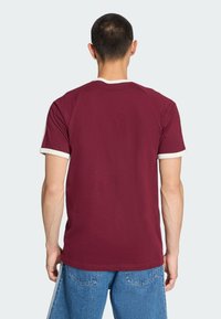 Μπορντό κοντομάνικο T-shirt με λευκή διακόσμηση, βαμβακερό ύφασμα, σχέδιο με στρογγυλή λαιμόκοψη και απαλή υφή. Η πίσω όψη δείχνει λεπτομέρειες στη ραφή των ώμων.