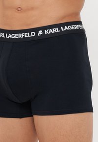 Fekete boxer alsónadrág puha pamutból. Fehér, fekete részletekkel ellátott logózott elasztikus derékrésszel rendelkezik. Testhez simuló fazon, sima textúra.