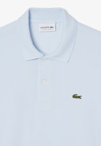 Polo shirt azzurro chiaro in cotone, con vestibilità classica, due bottoni al colletto e un piccolo logo di coccodrillo verde sul petto.