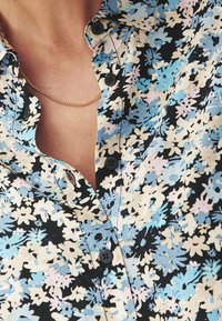 Květinová košile s modrými, bílými a růžovými vzory na černém pozadí. Obsahuje límec na knoflíky a černé knoflíky.