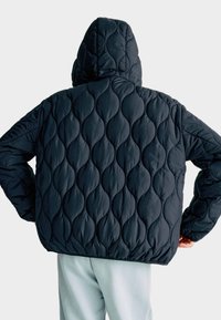 Kurtka puchowa w ciemnym granacie, z pikowaną teksturą z zaokrąglonymi kształtami. Posiada kaptur i elastyczne mankiety oraz luźny krój.