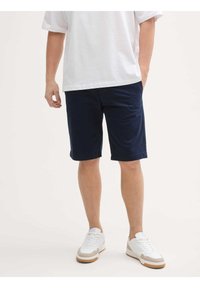 Marineblaue Shorts aus Baumwollmischung, mit lockerer Passform, geradem Schnitt und aufgesetzten Taschen. Kombiniert mit weißen Sportsneakern.