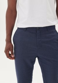 Pantalones texturizados azul marino con un corte slim, que presentan un cierre de botón y bolsillos laterales, combinados con una camiseta blanca lisa.