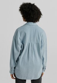 Camicia in corduroy azzurro chiaro con colletto, texture a coste visibili e polsini button-down. Presenta un yoke e dettagli a piega sul retro.