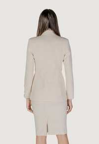 Blazer beige su misura con maniche lunghe, una silhouette aderente e un design con spacco sul retro, abbinato a una gonna abbinata al ginocchio.