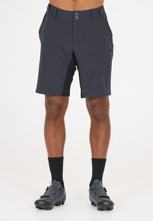 Dunkelgraue Shorts mit einem schlanken Design, strukturiertem Bündchen, vorderem Knopfverschluss und seitlichen Taschen. Tragen mit schwarzen Fahrradschuhen und Socken.