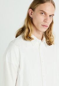 Chemise blanche à boutons, en coton, avec un col et des manches longues. Texture subtile avec un design minimaliste.