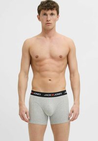 Pilki bokso apatiniai su juodu diržu, kuriame raudonai užrašyta prekės ženklo pavadinimas "JACK & JONES". Medvilnė, prigludusi forma, iki vidurio šlaunų.