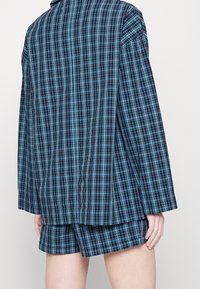 Modrá kostkovaná košile s krátkým rukávem a odpovídajícími kraťasy, v odstínech modré a námořnické, vyrobená z lehké látky.